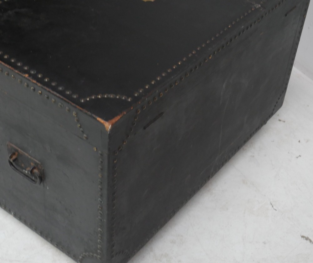 A black leather-covered storage trunk adorned with brass studding in festoon drape patterns, featuring side handles and castors. View VIII