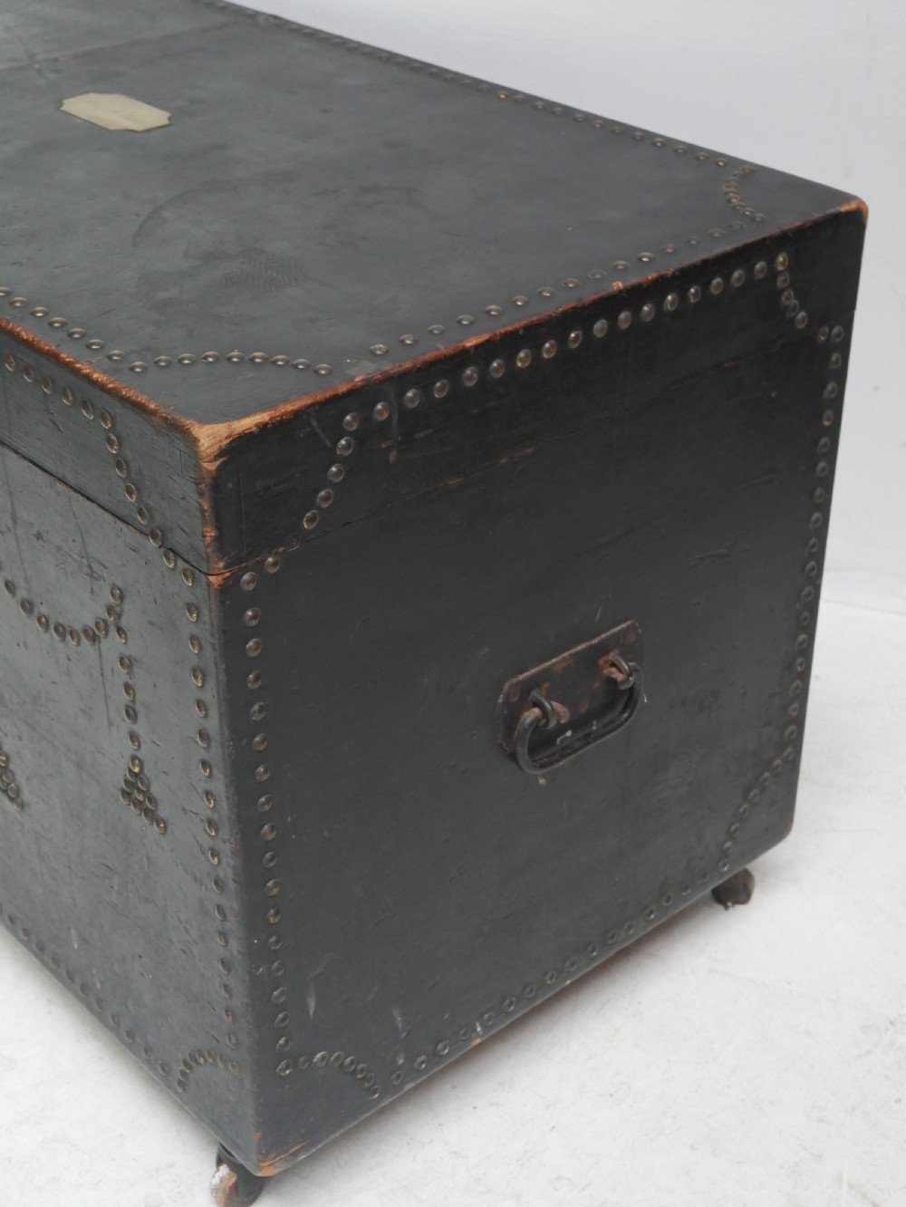 A black leather-covered storage trunk adorned with brass studding in festoon drape patterns, featuring side handles and castors. View IX