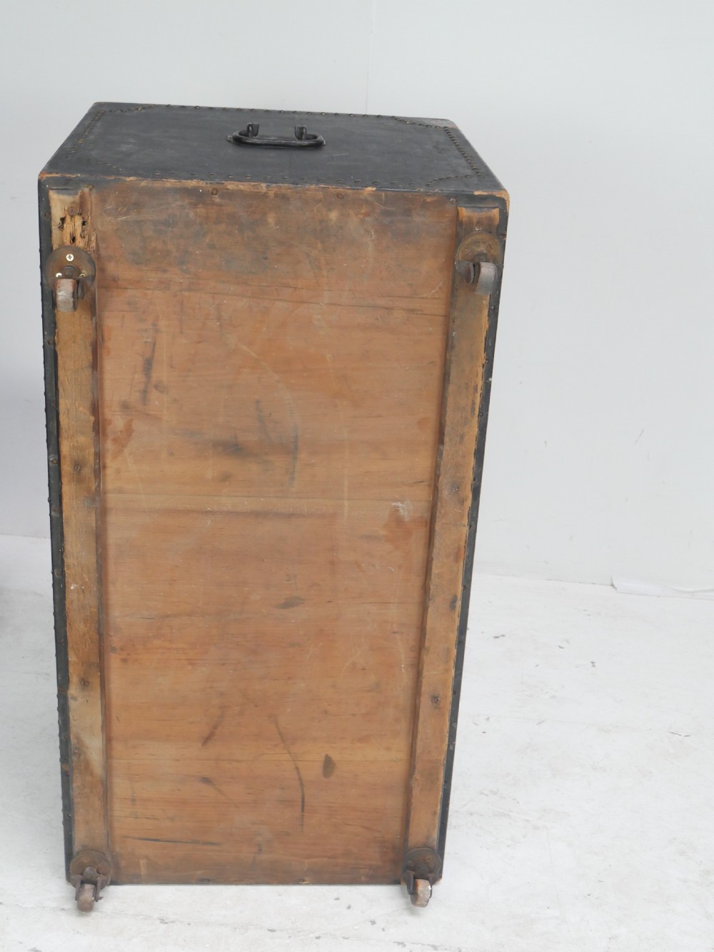 A black leather-covered storage trunk adorned with brass studding in festoon drape patterns, featuring side handles and castors. View XIII