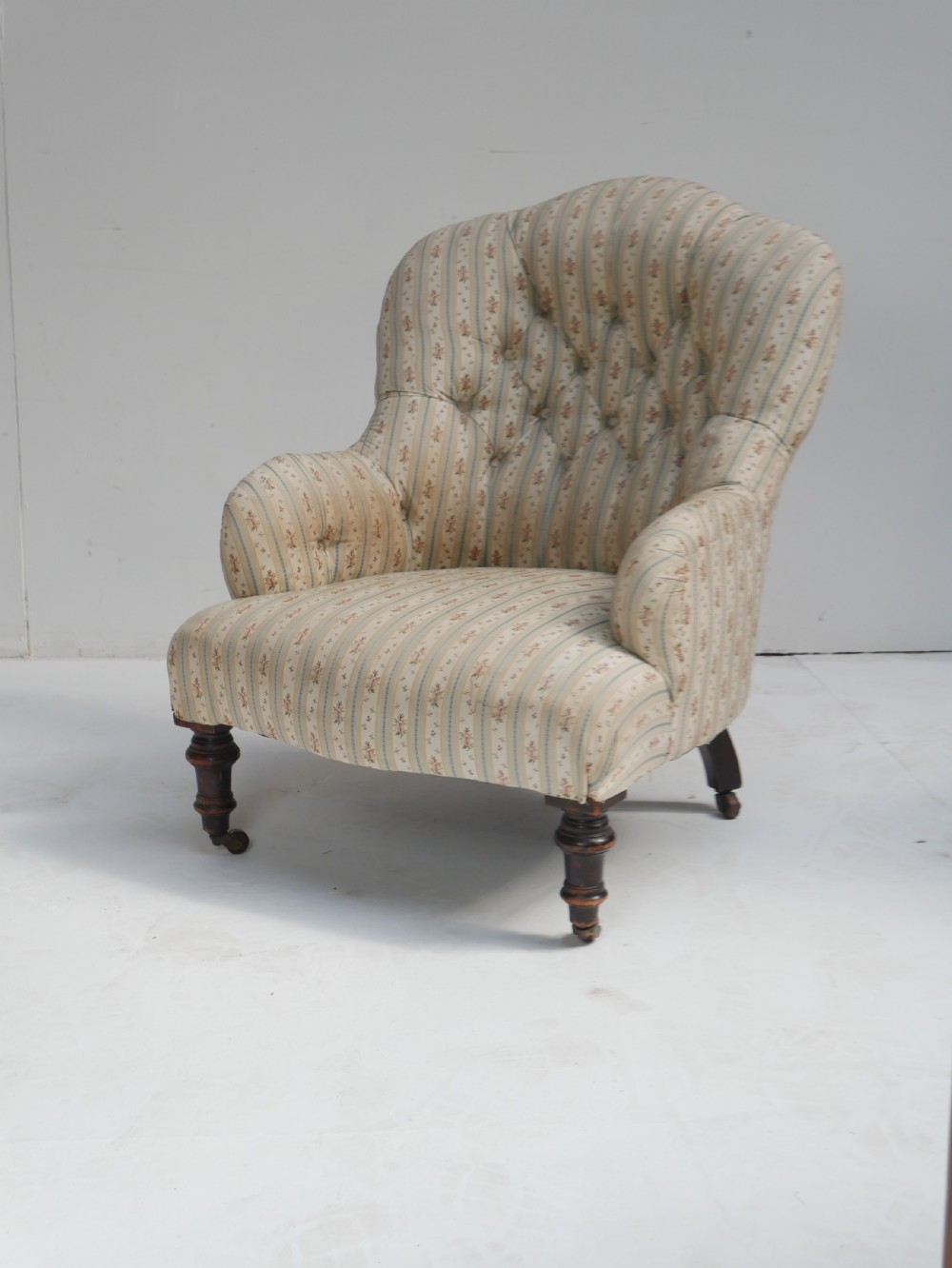 A low Victorian button-backed armchair upholstered in beige floral striped fabric with turned mahogany front legs on castors.