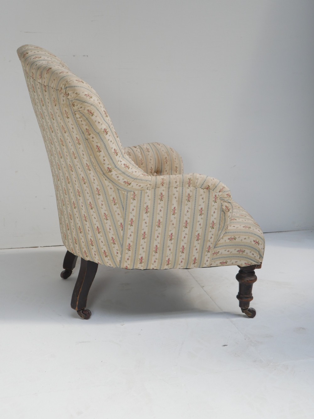 A low Victorian button-backed armchair upholstered in beige floral striped fabric with turned mahogany front legs on castors. View II