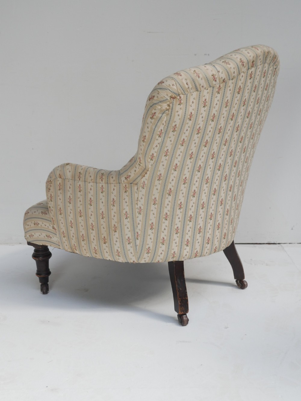 A low Victorian button-backed armchair upholstered in beige floral striped fabric with turned mahogany front legs on castors. View III