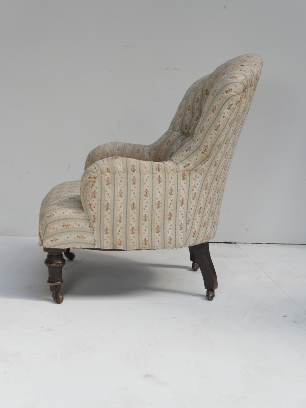 A low Victorian button-backed armchair upholstered in beige floral striped fabric with turned mahogany front legs on castors. View IV