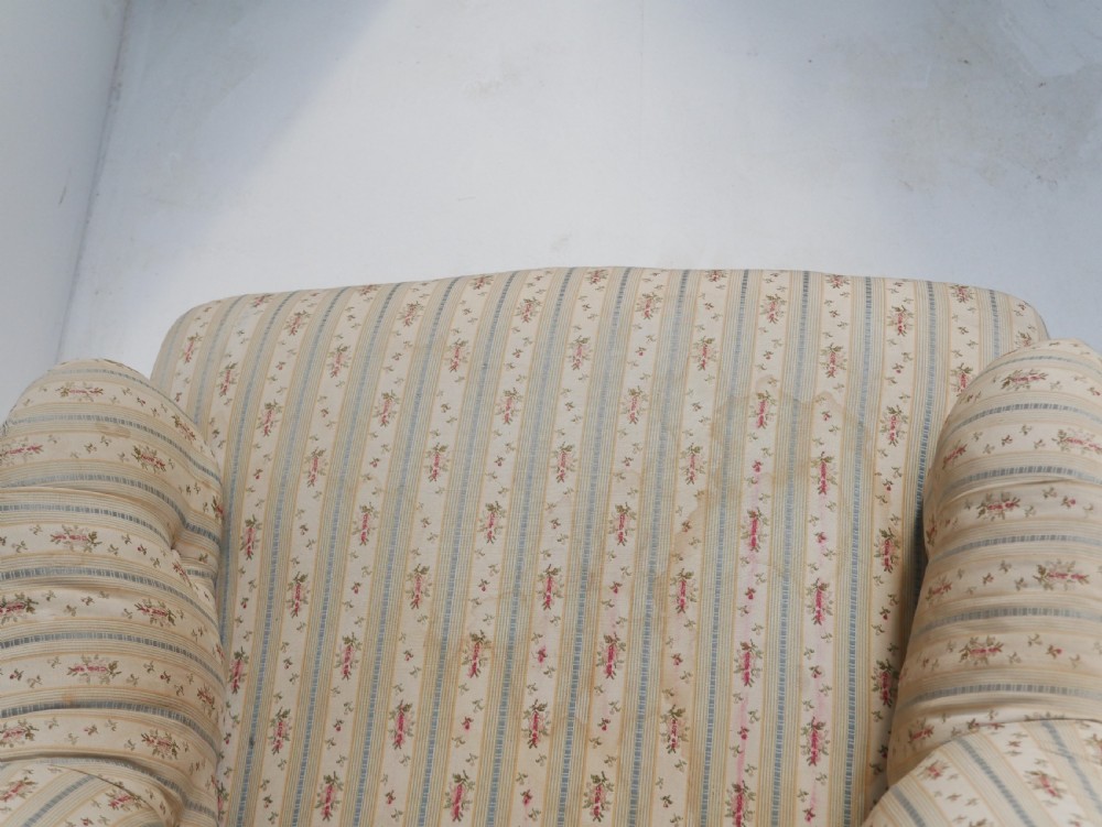 A low Victorian button-backed armchair upholstered in beige floral striped fabric with turned mahogany front legs on castors. View IX
