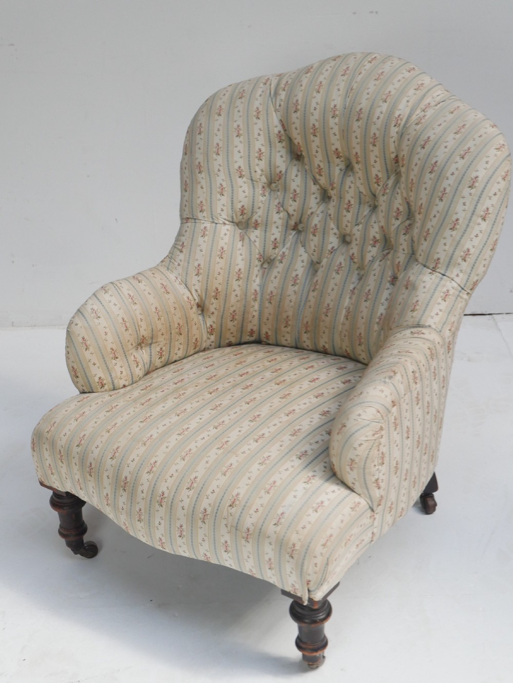 A low Victorian button-backed armchair upholstered in beige floral striped fabric with turned mahogany front legs on castors. View X