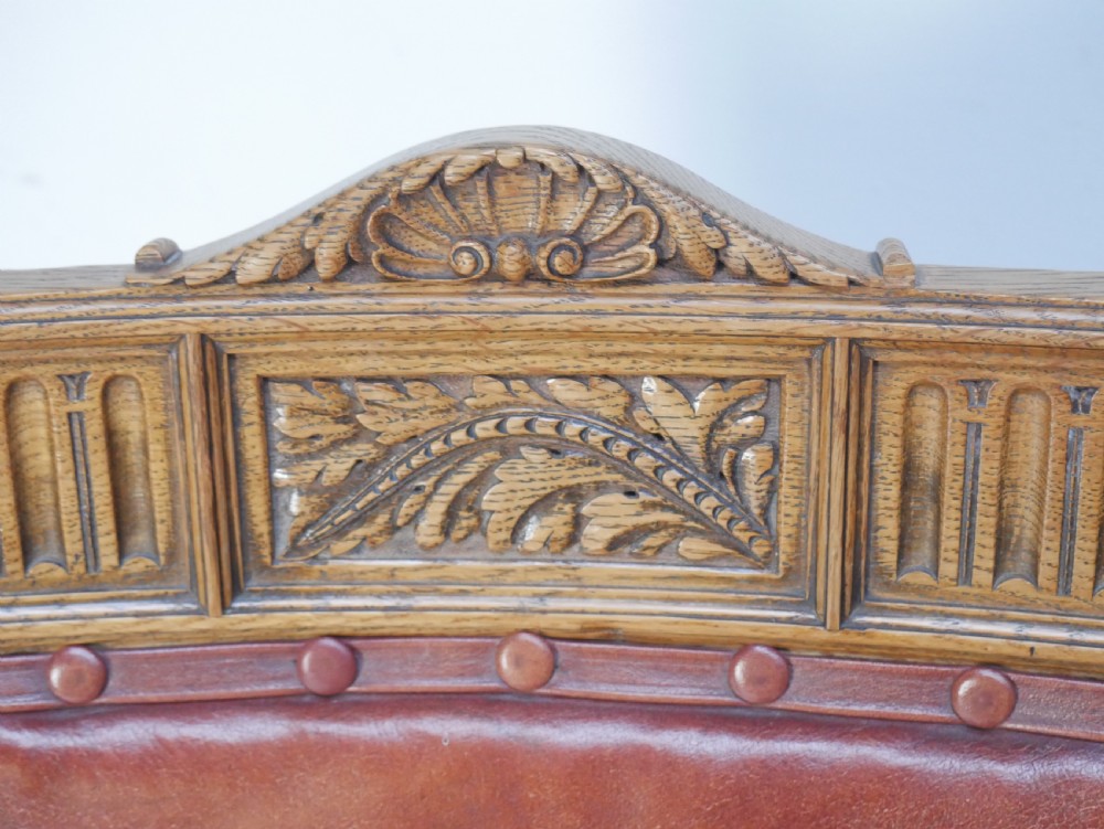 A pair of Victorian carved oak side chairs featuring reddish-brown leather seats and backrests secured with brass studs, set on turned front legs with castors. View II