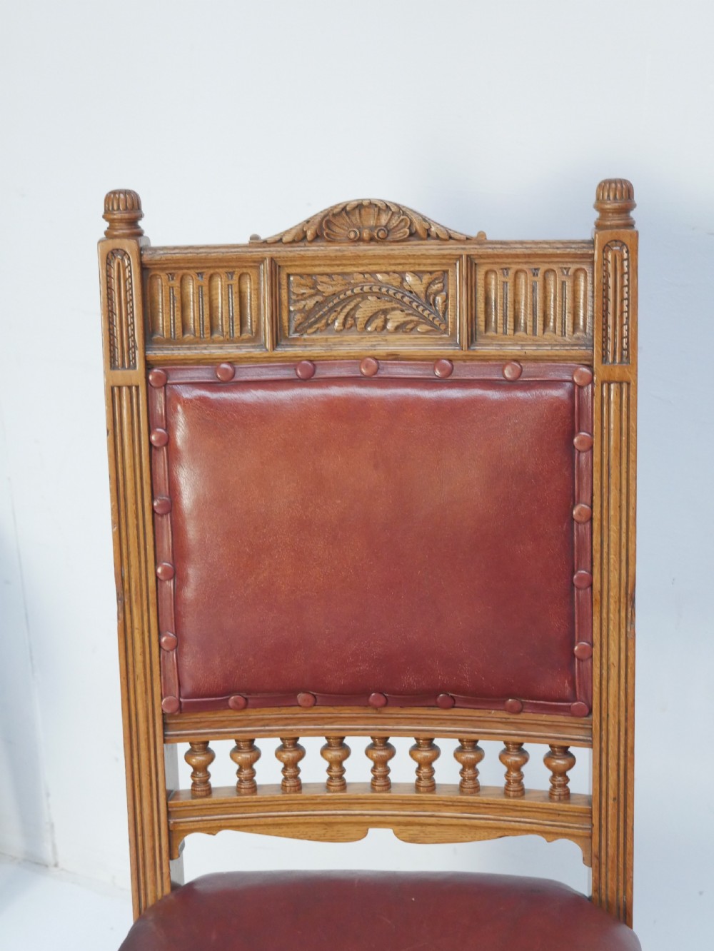 A pair of Victorian carved oak side chairs featuring reddish-brown leather seats and backrests secured with brass studs, set on turned front legs with castors. View III