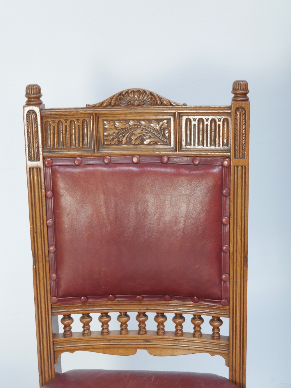 A pair of Victorian carved oak side chairs featuring reddish-brown leather seats and backrests secured with brass studs, set on turned front legs with castors. View IV