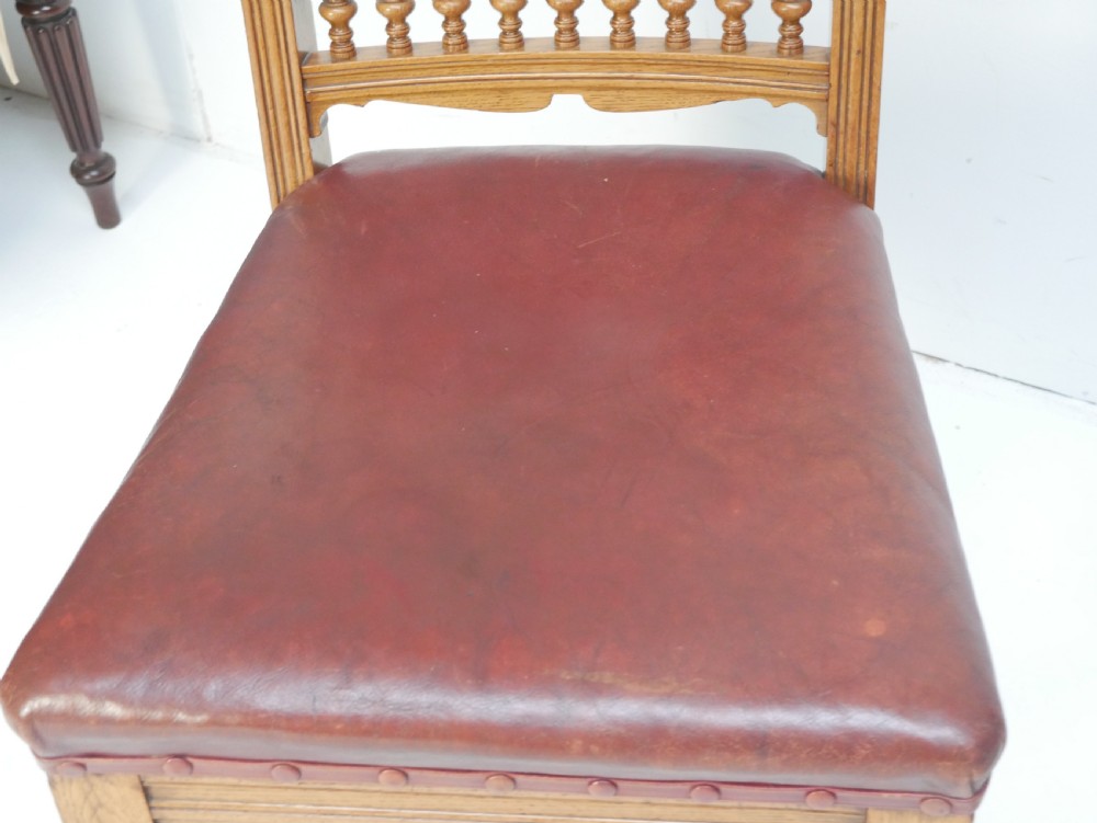 A pair of Victorian carved oak side chairs featuring reddish-brown leather seats and backrests secured with brass studs, set on turned front legs with castors. View VI