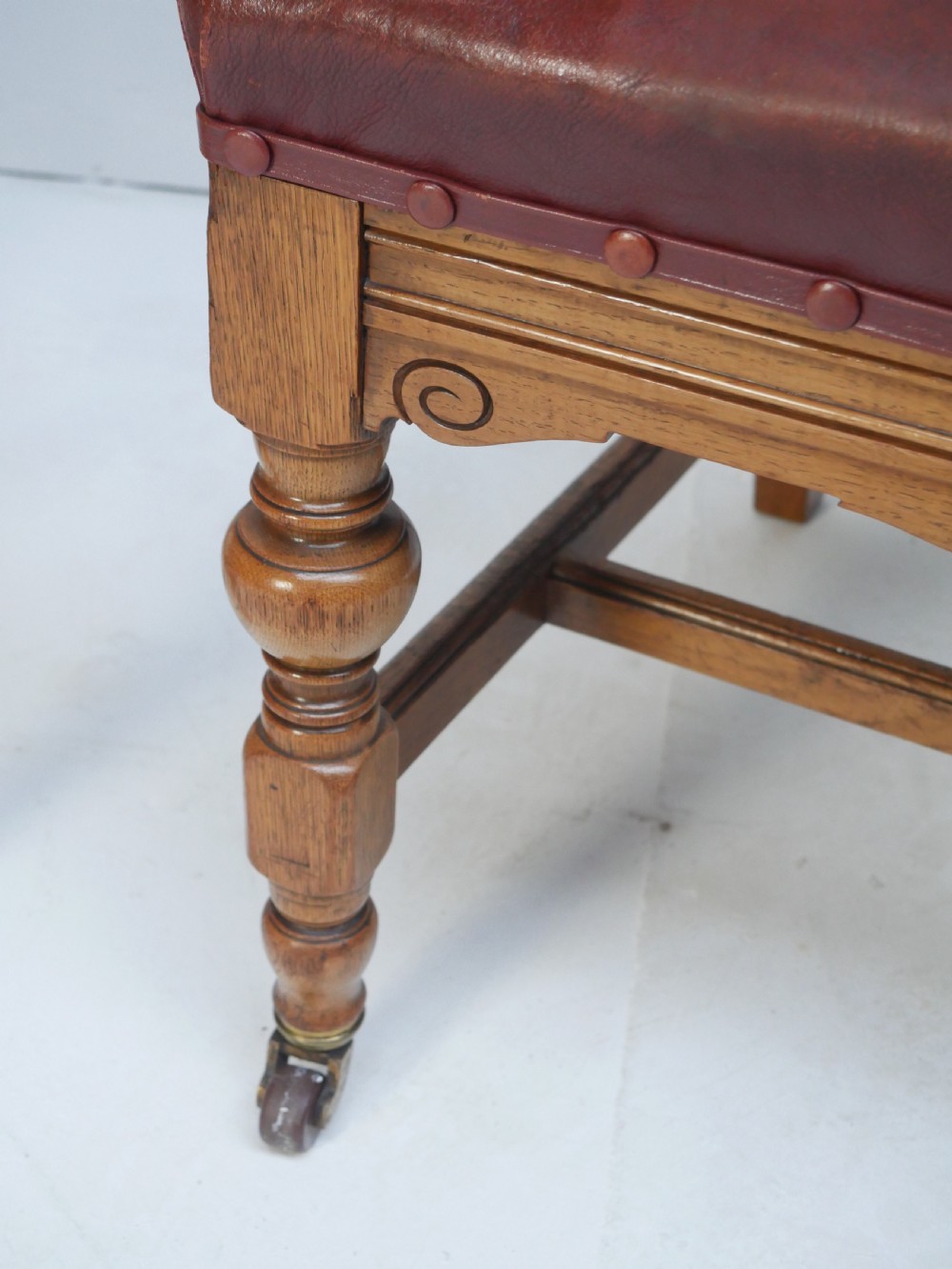 A pair of Victorian carved oak side chairs featuring reddish-brown leather seats and backrests secured with brass studs, set on turned front legs with castors. View VII
