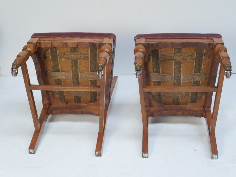 A pair of Victorian carved oak side chairs featuring reddish-brown leather seats and backrests secured with brass studs, set on turned front legs with castors. View VIII