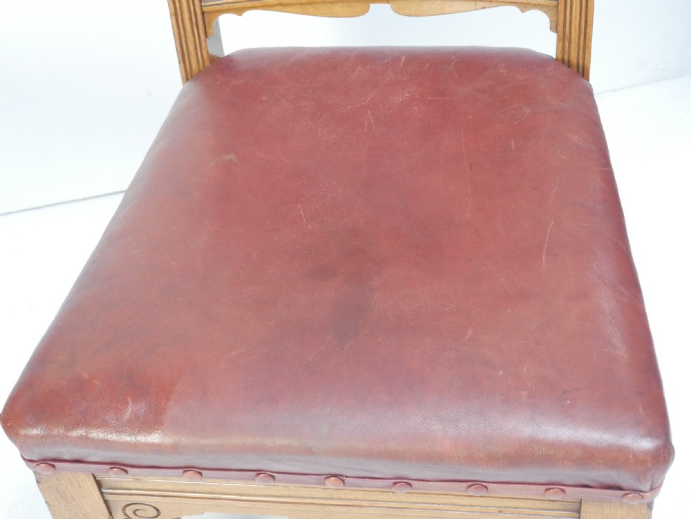 A pair of Victorian carved oak side chairs featuring reddish-brown leather seats and backrests secured with brass studs, set on turned front legs with castors. View XI
