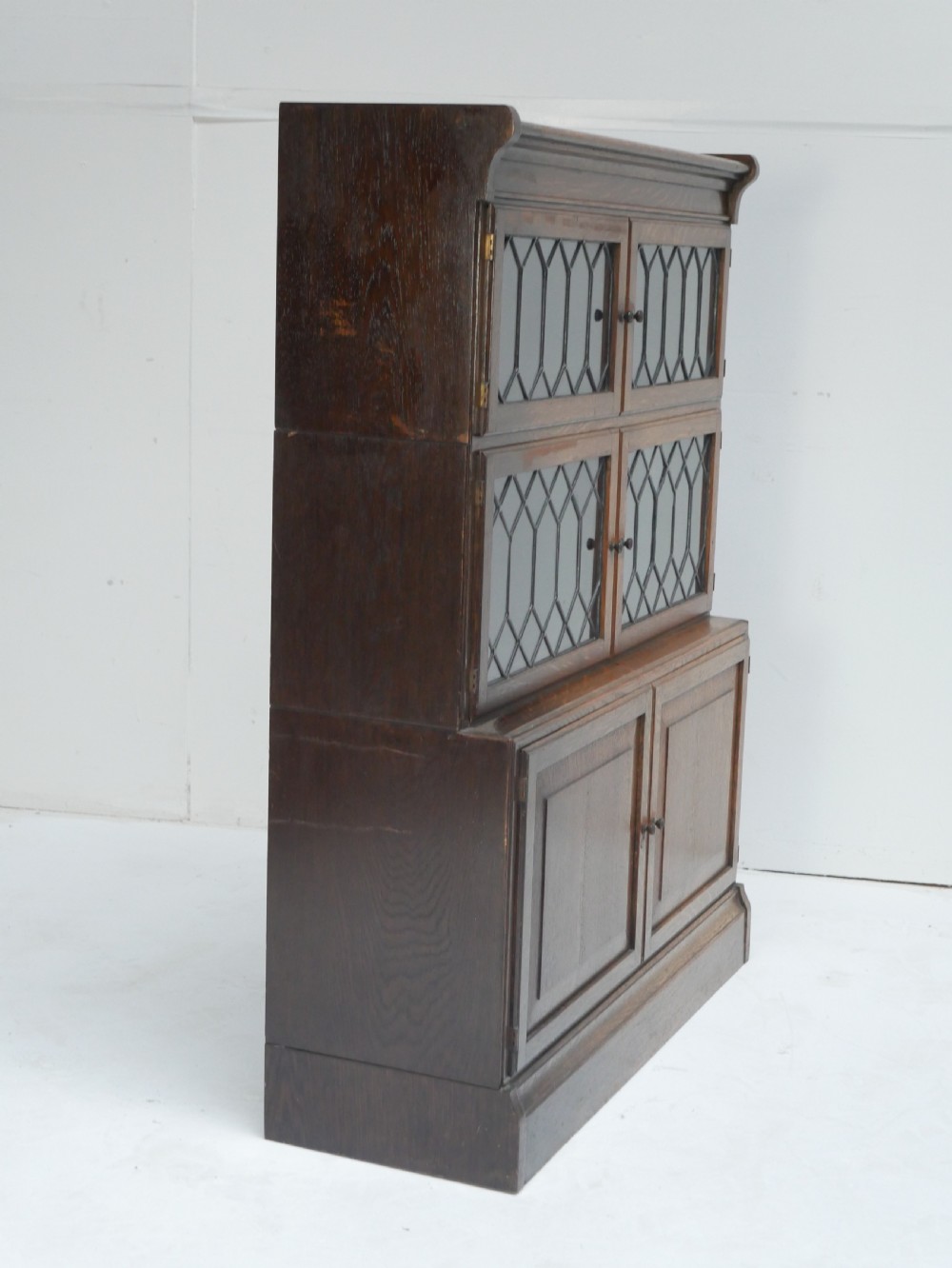 An oak stacking bookcase featuring two upper tiers with double diamond-pattern leaded glass doors above a lower cupboard with two solid panelled wooden doors. View III