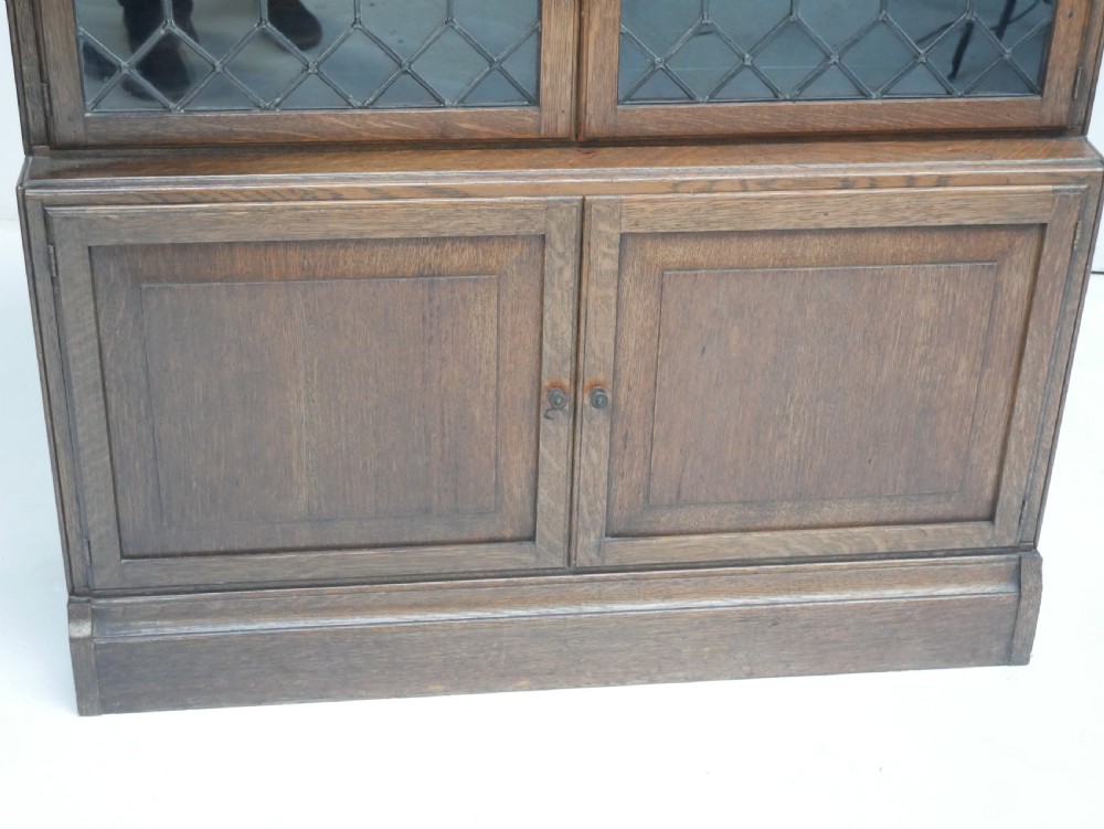 An oak stacking bookcase featuring two upper tiers with double diamond-pattern leaded glass doors above a lower cupboard with two solid panelled wooden doors. View V