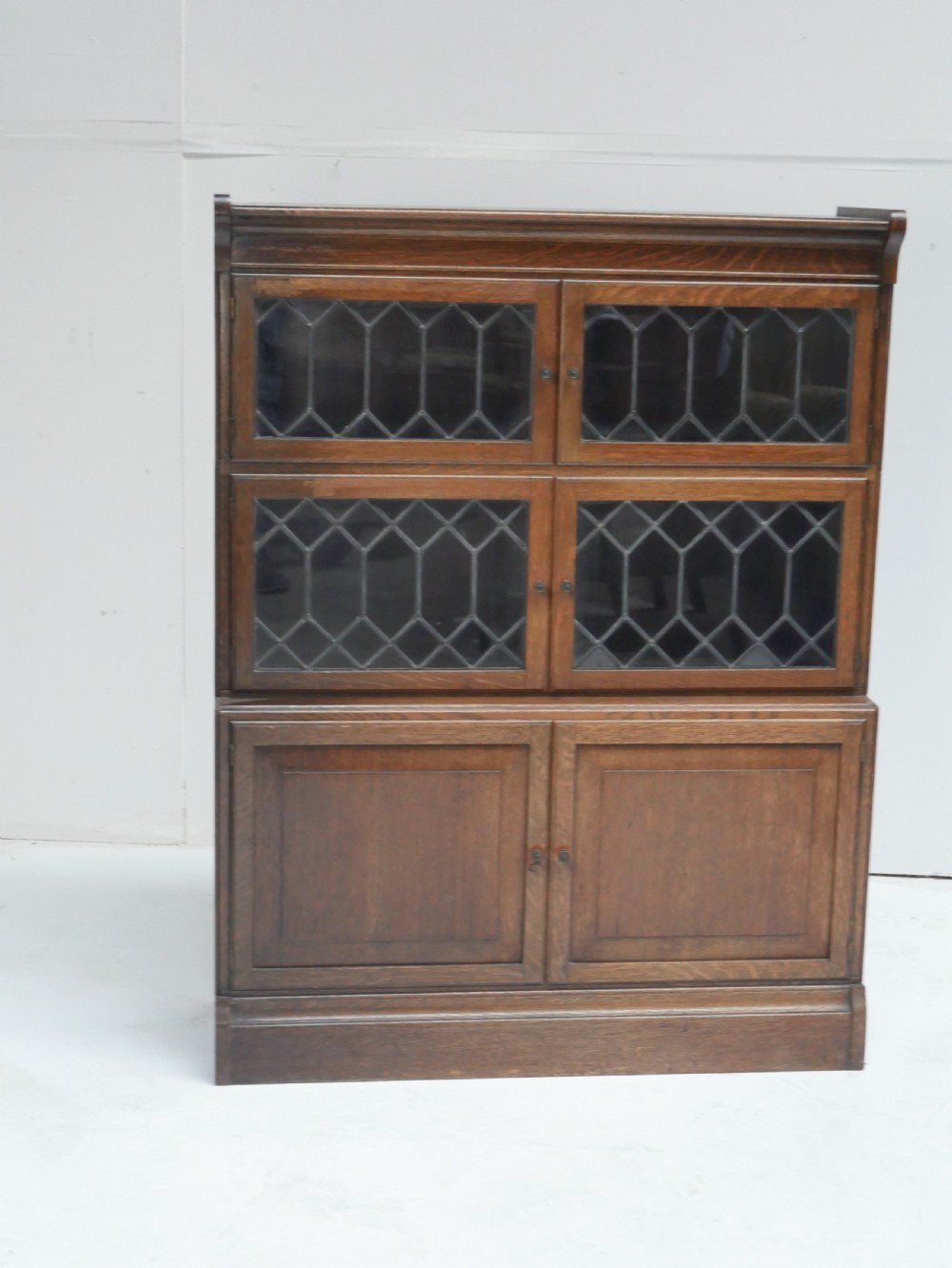 An oak stacking bookcase featuring two upper tiers with double diamond-pattern leaded glass doors above a lower cupboard with two solid panelled wooden doors. View IX
