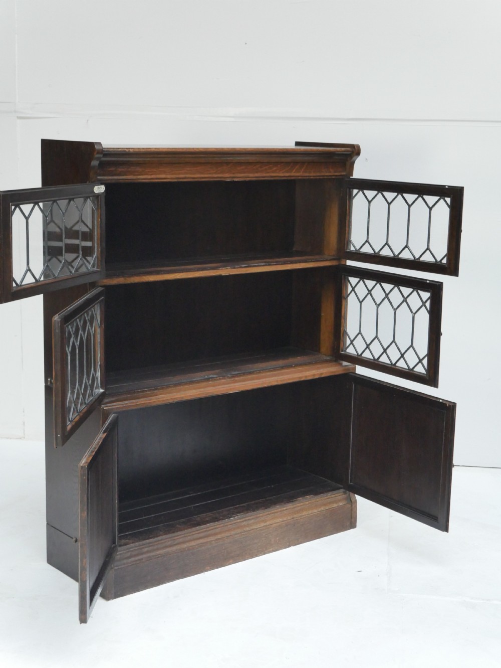 An oak stacking bookcase featuring two upper tiers with double diamond-pattern leaded glass doors above a lower cupboard with two solid panelled wooden doors. View X