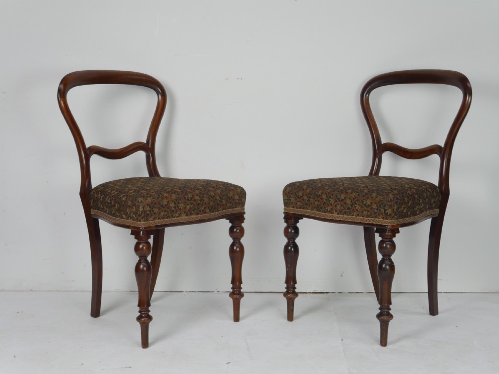 A pair of Victorian rosewood balloon back side chairs featuring turned front legs and patterned upholstered seats.
