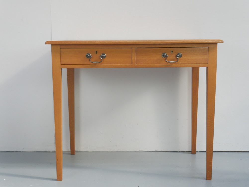 A golden oak writing table with two frieze drawers fitted with brass drop handles, raised on four square tapered legs.