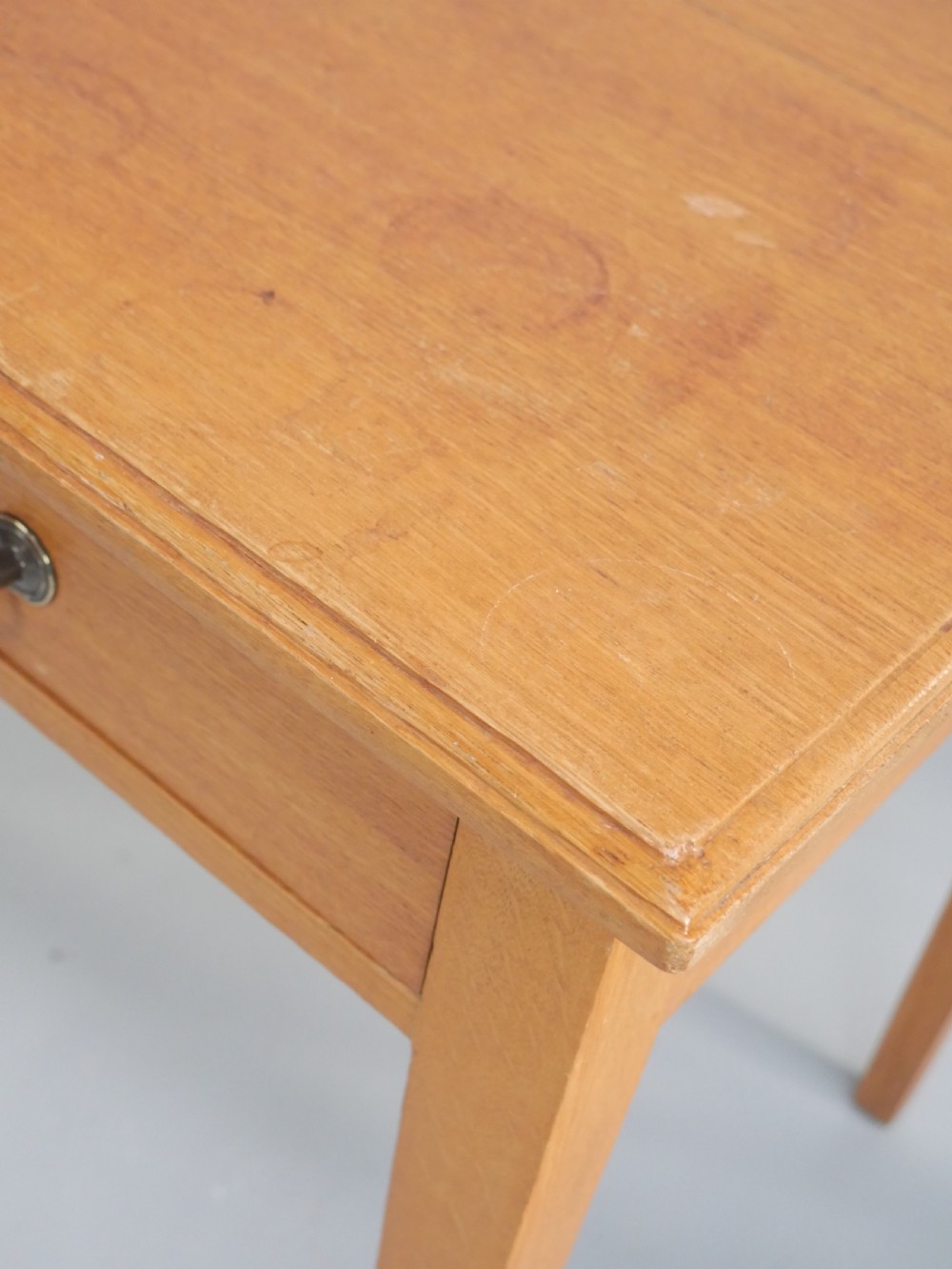 A golden oak writing table with two frieze drawers fitted with brass drop handles, raised on four square tapered legs. View IV