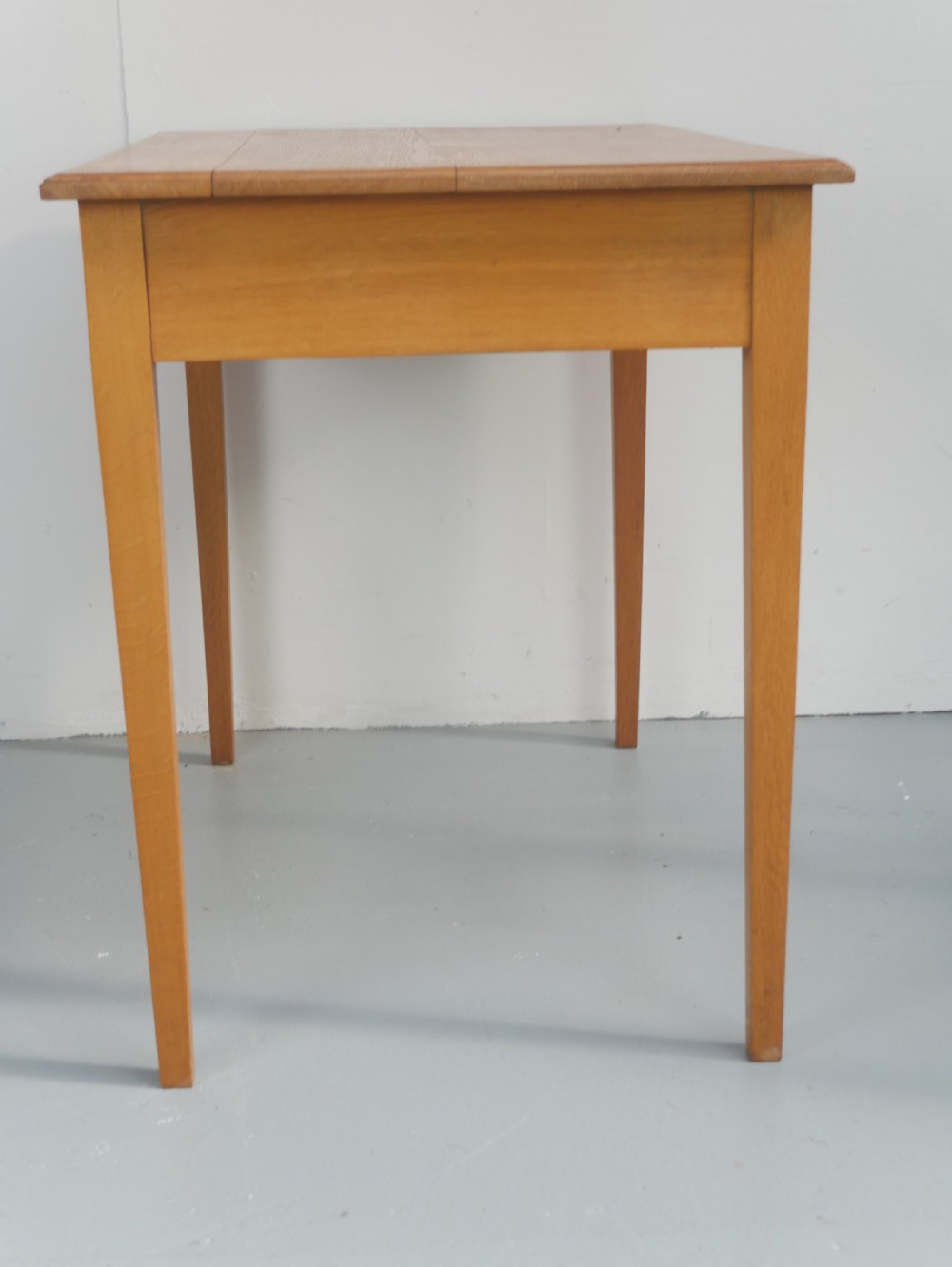 A golden oak writing table with two frieze drawers fitted with brass drop handles, raised on four square tapered legs. View IX
