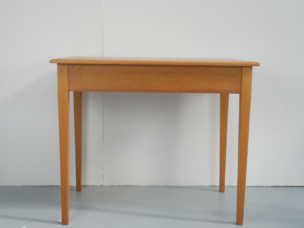 A golden oak writing table with two frieze drawers fitted with brass drop handles, raised on four square tapered legs. View XIII