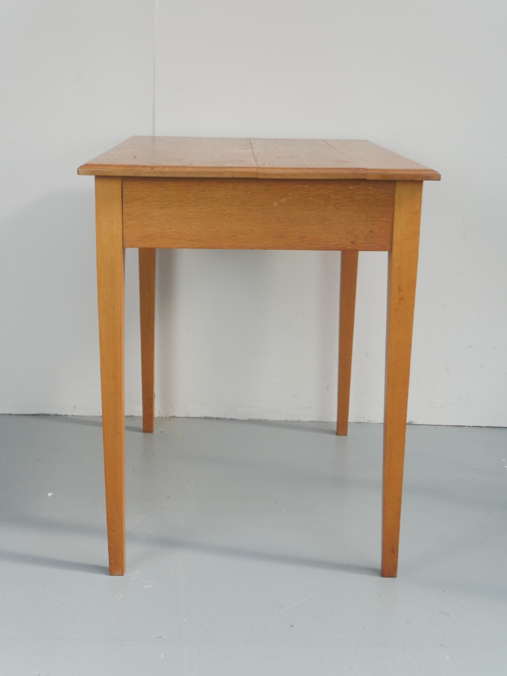 A golden oak writing table with two frieze drawers fitted with brass drop handles, raised on four square tapered legs. View XIV