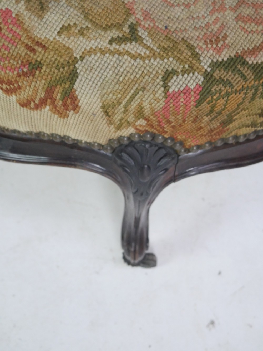 An oval upholstered stool featuring dark carved wooden cabriole legs with castors and a floral needlepoint fabric top. View IV