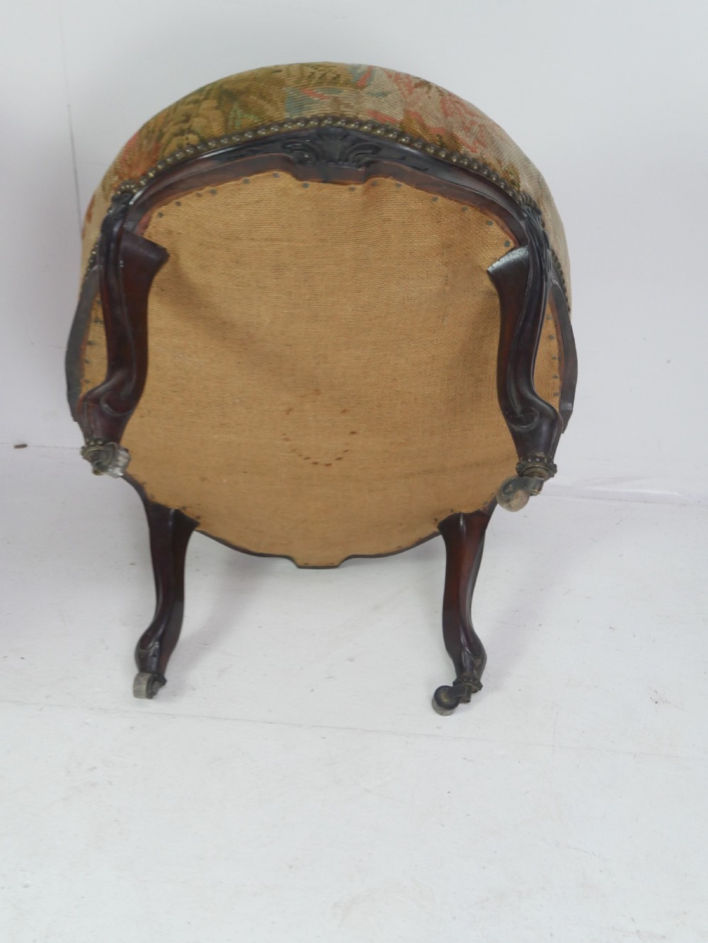 An oval upholstered stool featuring dark carved wooden cabriole legs with castors and a floral needlepoint fabric top. View VI