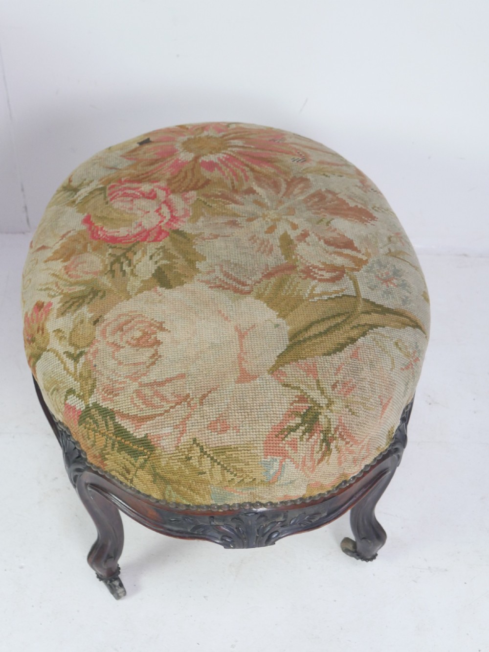 An oval upholstered stool featuring dark carved wooden cabriole legs with castors and a floral needlepoint fabric top. View XIII