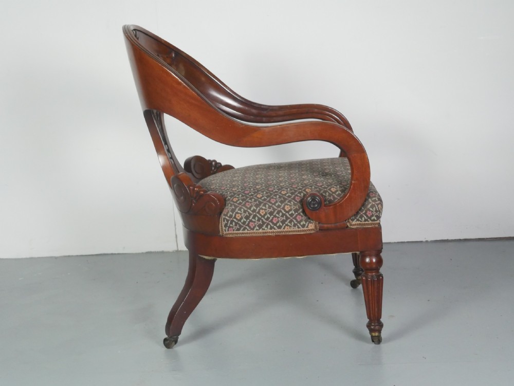 A dark mahogany Regency armchair with a carved leaf back splat, open scrolled arms, patterned upholstered seat, and turned front legs with brass castors. View III