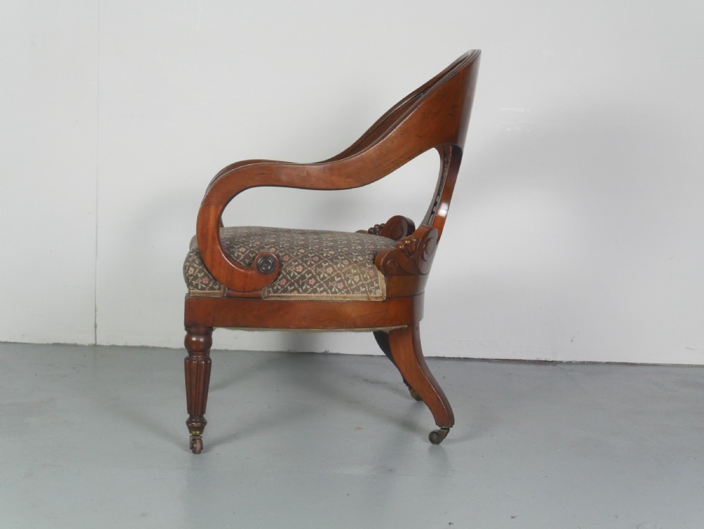 A dark mahogany Regency armchair with a carved leaf back splat, open scrolled arms, patterned upholstered seat, and turned front legs with brass castors. View VI