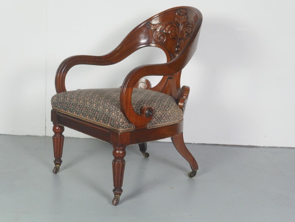 A dark mahogany Regency armchair with a carved leaf back splat, open scrolled arms, patterned upholstered seat, and turned front legs with brass castors. View VII