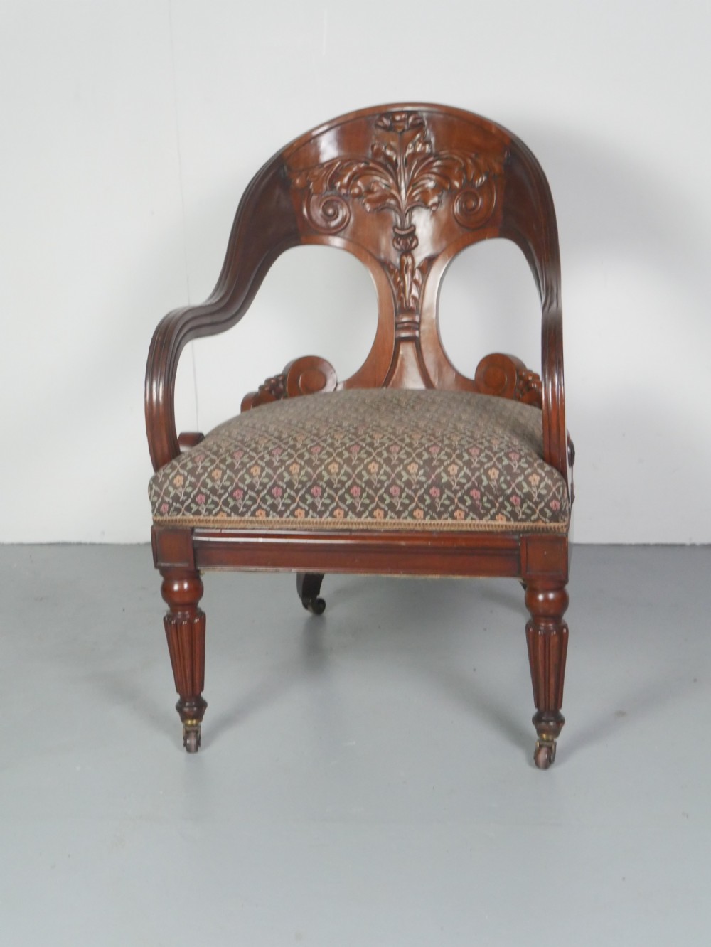 A dark mahogany Regency armchair with a carved leaf back splat, open scrolled arms, patterned upholstered seat, and turned front legs with brass castors. View VIII