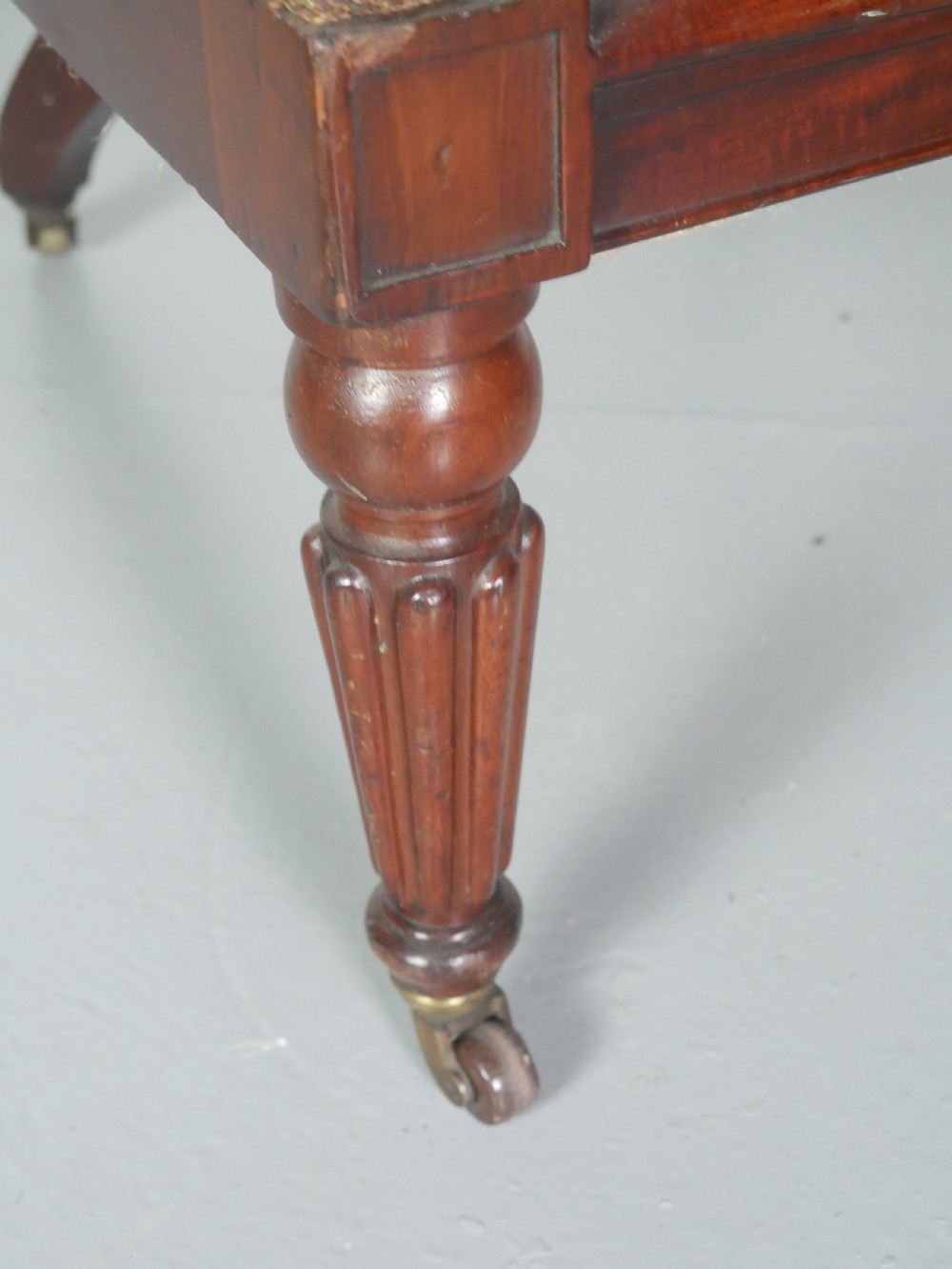 A dark mahogany Regency armchair with a carved leaf back splat, open scrolled arms, patterned upholstered seat, and turned front legs with brass castors. View IX