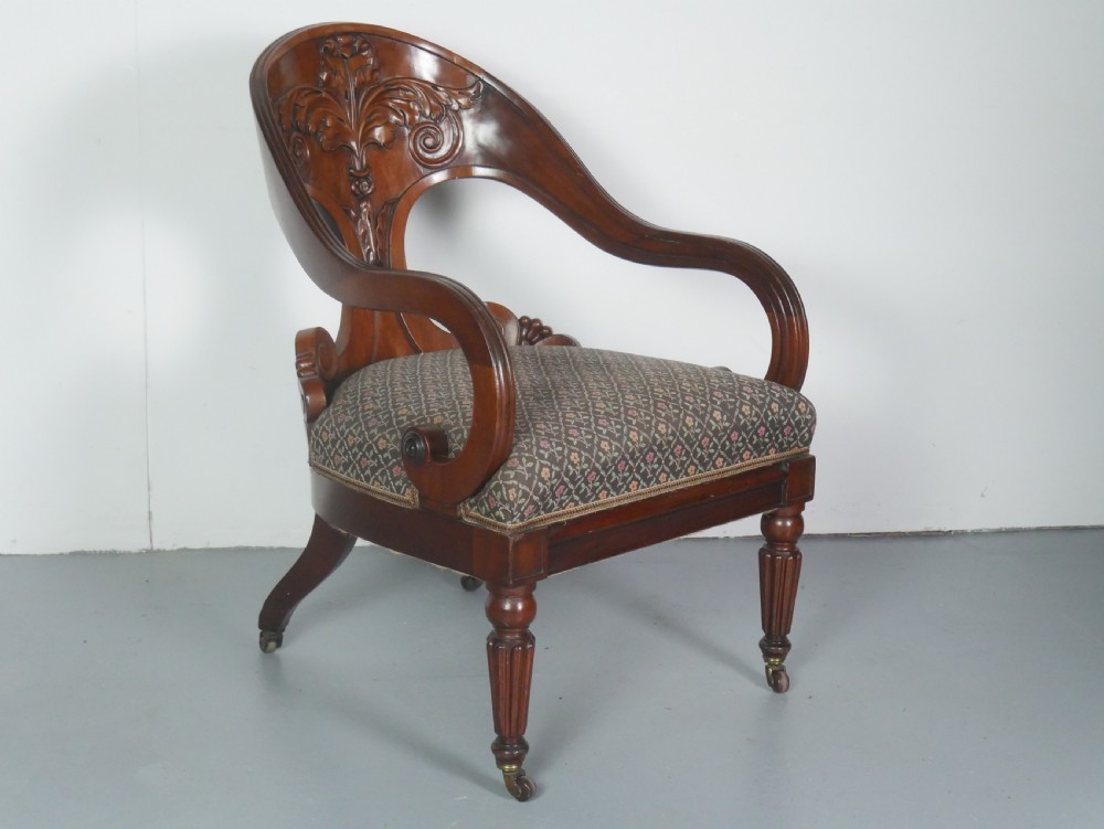 A dark mahogany Regency armchair with a carved leaf back splat, open scrolled arms, patterned upholstered seat, and turned front legs with brass castors. View XII