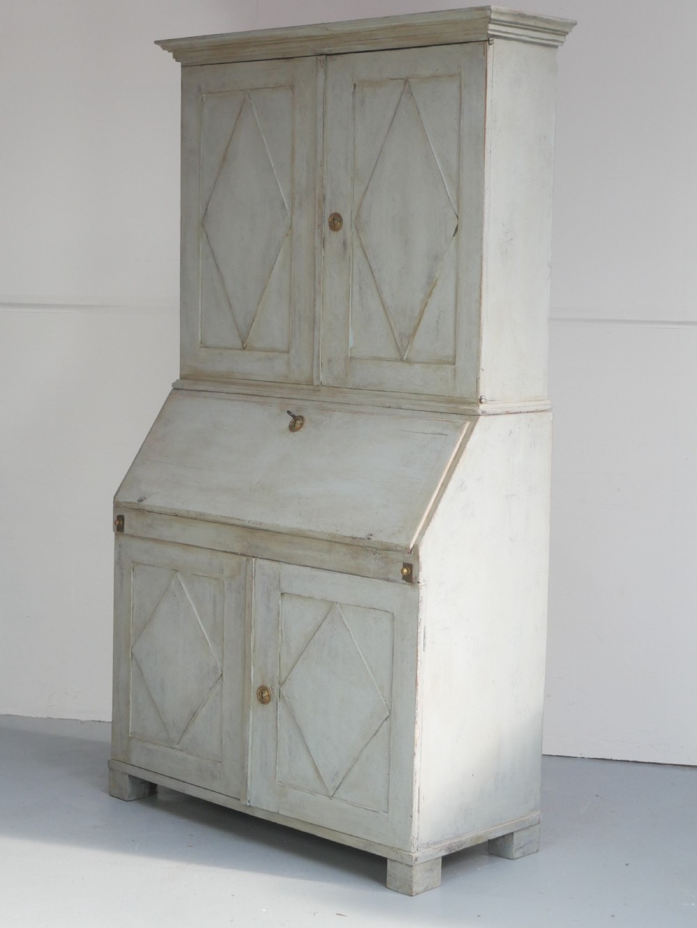 A tall two-tier Swedish softwood bureau cabinet with diamond panel moulding on the doors, a slanted fall-front flap, and a distressed pale grey painted finish.