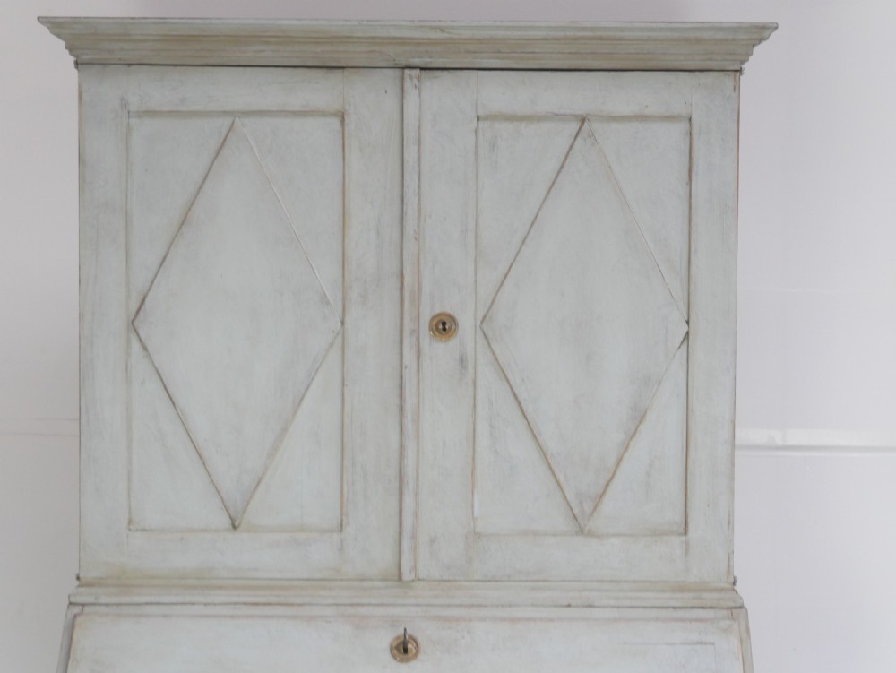 A tall two-tier Swedish softwood bureau cabinet with diamond panel moulding on the doors, a slanted fall-front flap, and a distressed pale grey painted finish. View X
