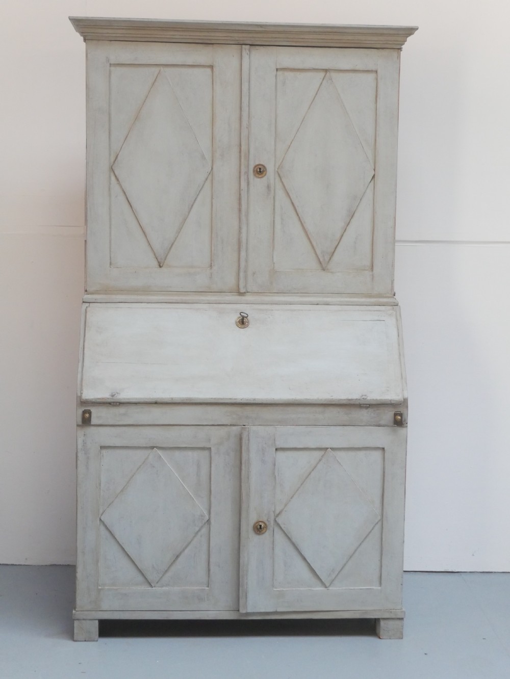 A tall two-tier Swedish softwood bureau cabinet with diamond panel moulding on the doors, a slanted fall-front flap, and a distressed pale grey painted finish. View XII
