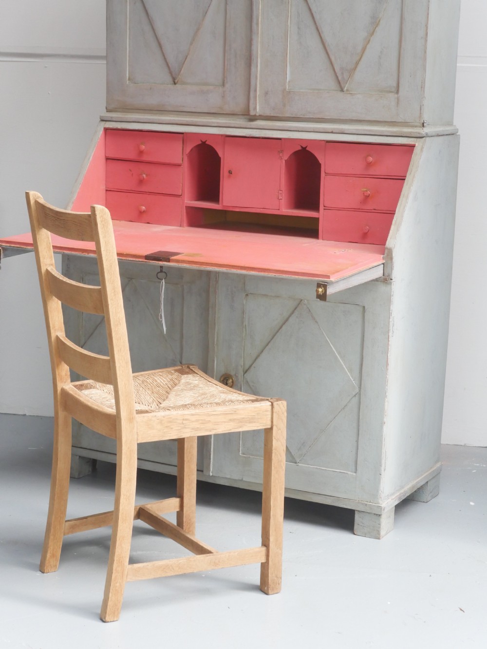 A tall two-tier Swedish softwood bureau cabinet with diamond panel moulding on the doors, a slanted fall-front flap, and a distressed pale grey painted finish. View II