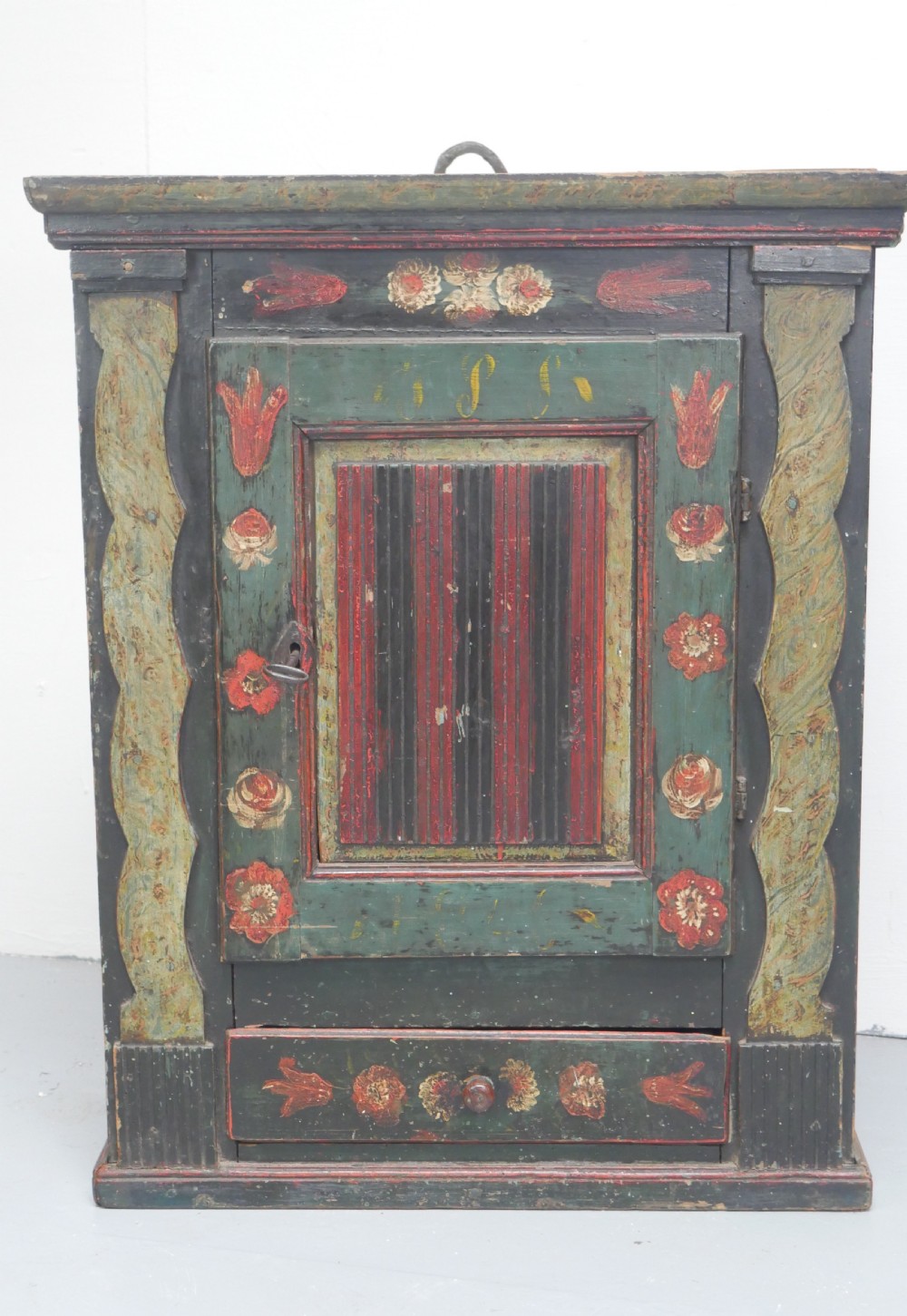 An antique dark green Swedish wall cupboard featuring hand-painted floral motifs, a central panel door, and a single lower drawer. View III
