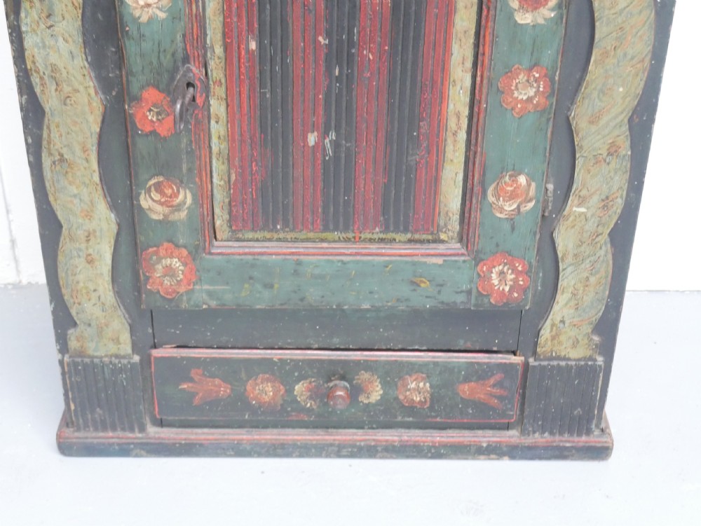 An antique dark green Swedish wall cupboard featuring hand-painted floral motifs, a central panel door, and a single lower drawer. View X