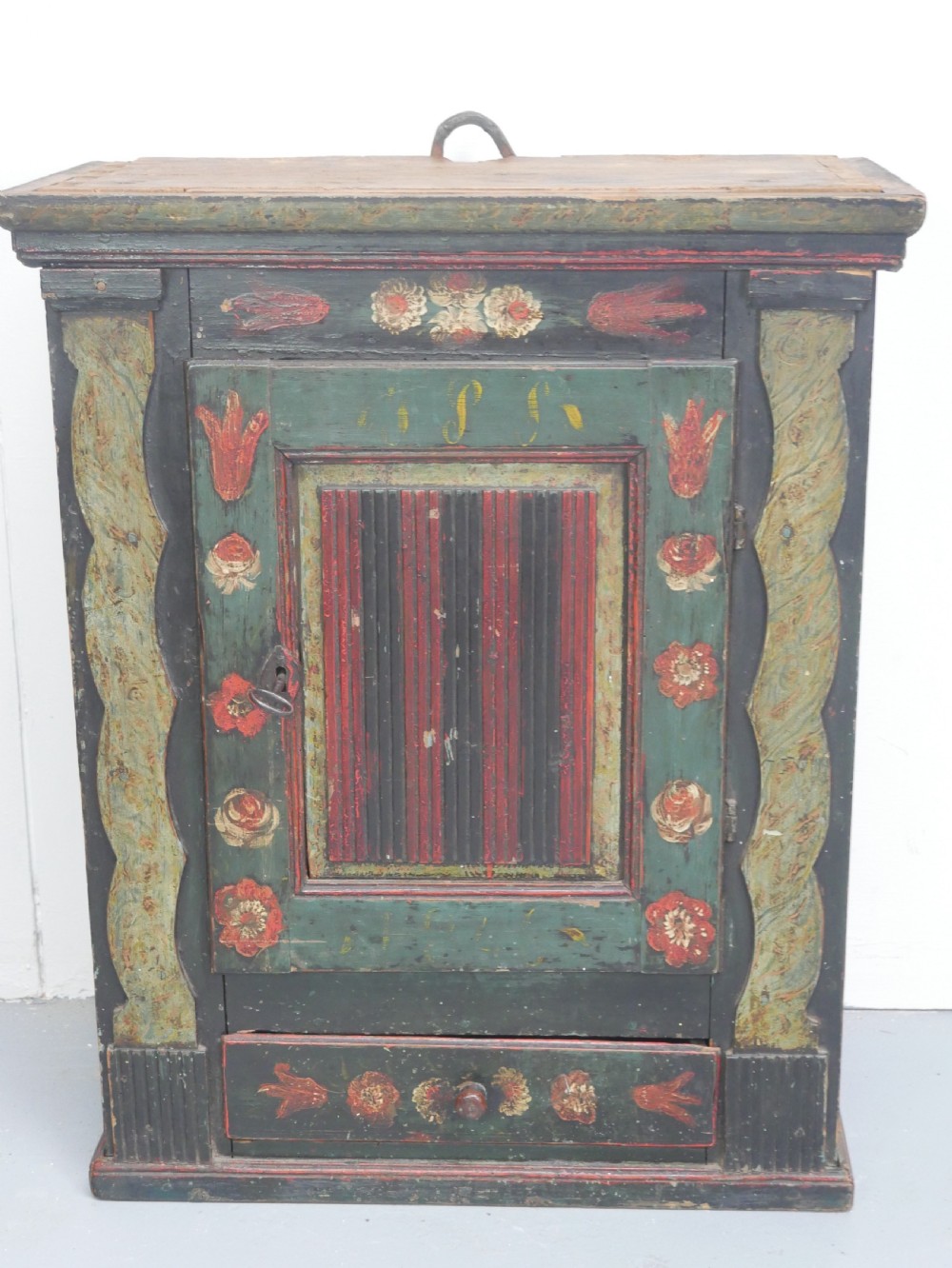 An antique dark green Swedish wall cupboard featuring hand-painted floral motifs, a central panel door, and a single lower drawer. View XVIII