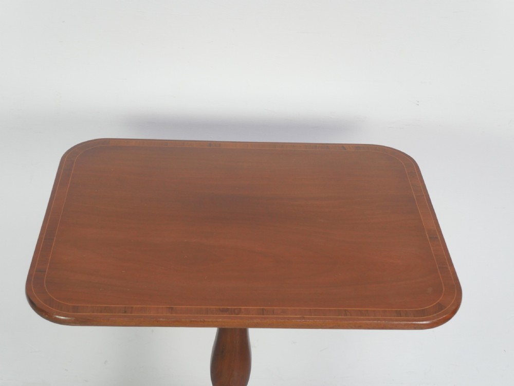 An antique mahogany tilt-top table with a rectangular inlaid tabletop raised vertically on a turned central pedestal and three curved legs. View II