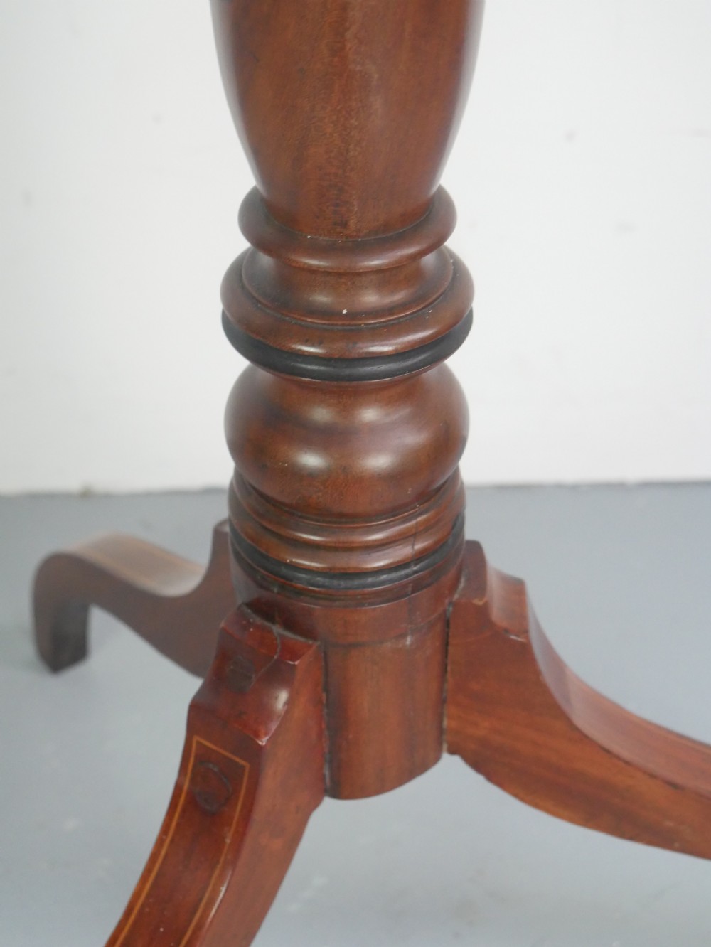 An antique mahogany tilt-top table with a rectangular inlaid tabletop raised vertically on a turned central pedestal and three curved legs. View IV