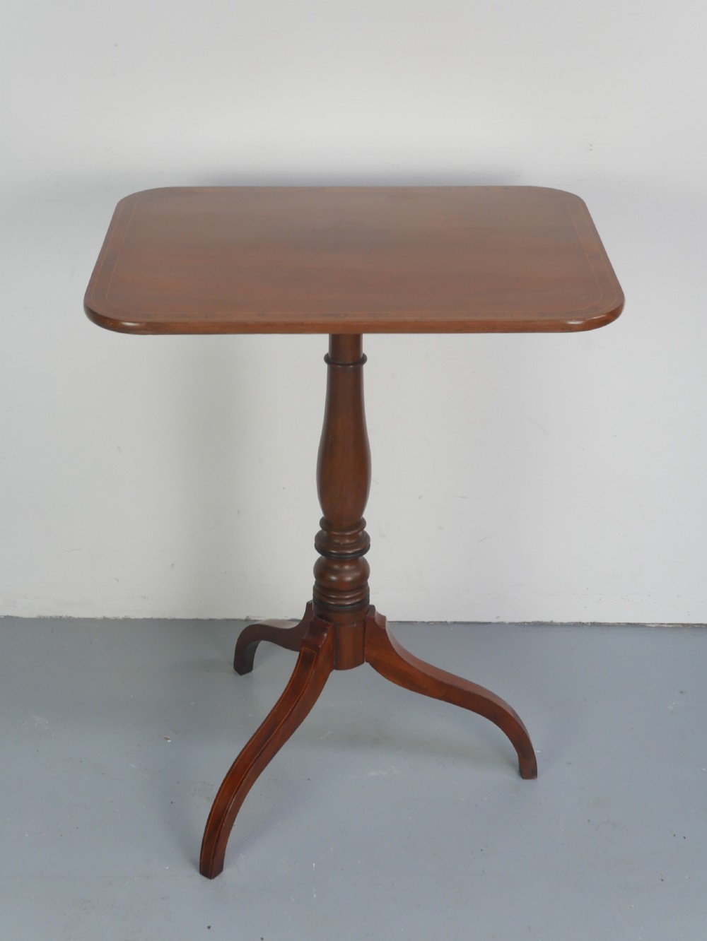 An antique mahogany tilt-top table with a rectangular inlaid tabletop raised vertically on a turned central pedestal and three curved legs. View VII