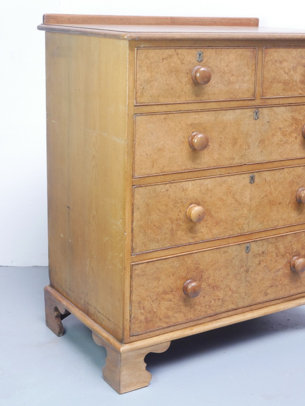 An antique burr ash chest of drawers featuring two short over three long graduated drawers with turned wooden knobs and bracket feet. View VIII