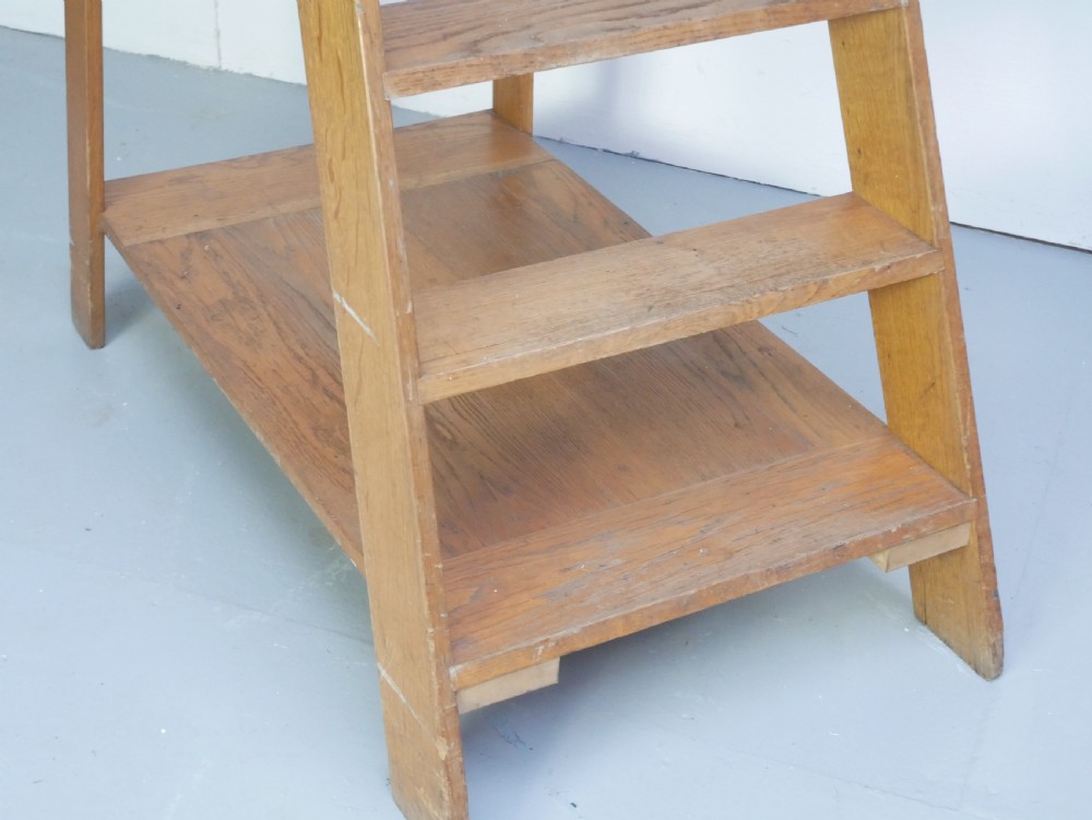 A tall freestanding oak library step ladder featuring multiple wide treads, shaped handholds at the top, and a warm natural wood finish. View II