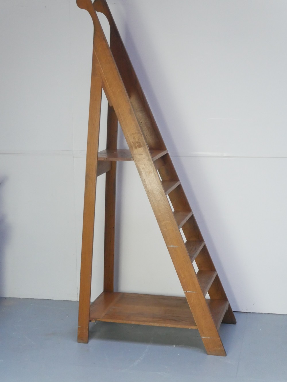 A tall freestanding oak library step ladder featuring multiple wide treads, shaped handholds at the top, and a warm natural wood finish. View VI