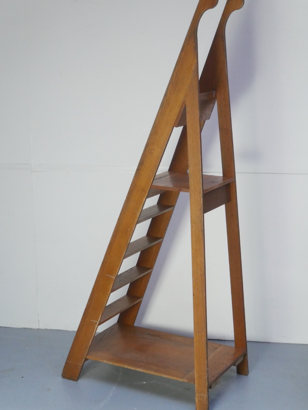 A tall freestanding oak library step ladder featuring multiple wide treads, shaped handholds at the top, and a warm natural wood finish. View XI