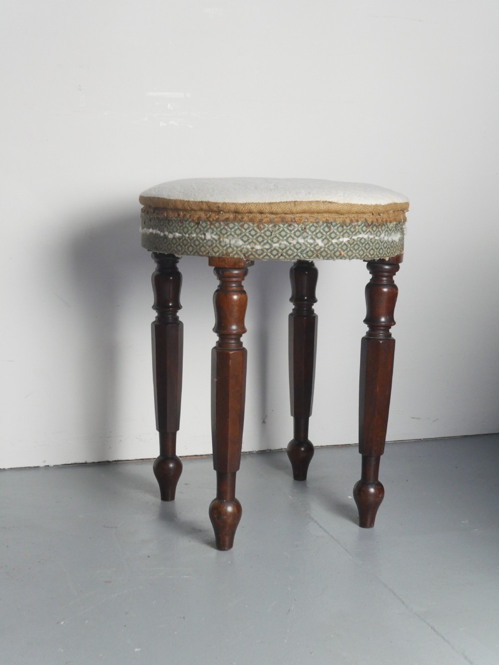 A circular stool with four dark turned timber legs and a padded circular top showing visible upholstery layers.